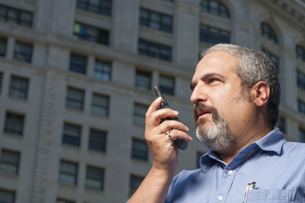 Man talking in front of Building on a walkie talkie